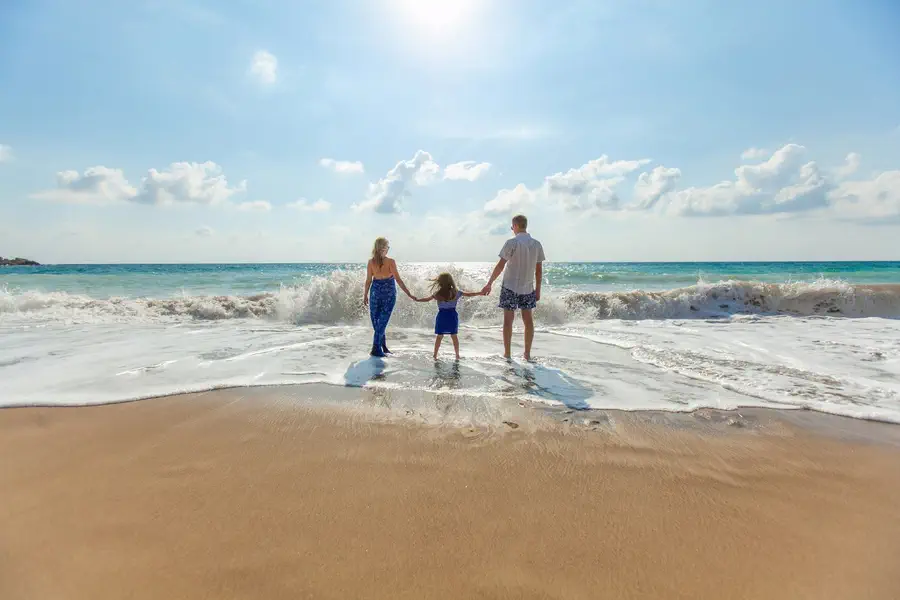 A family holding hands at the water's edge on a bright day