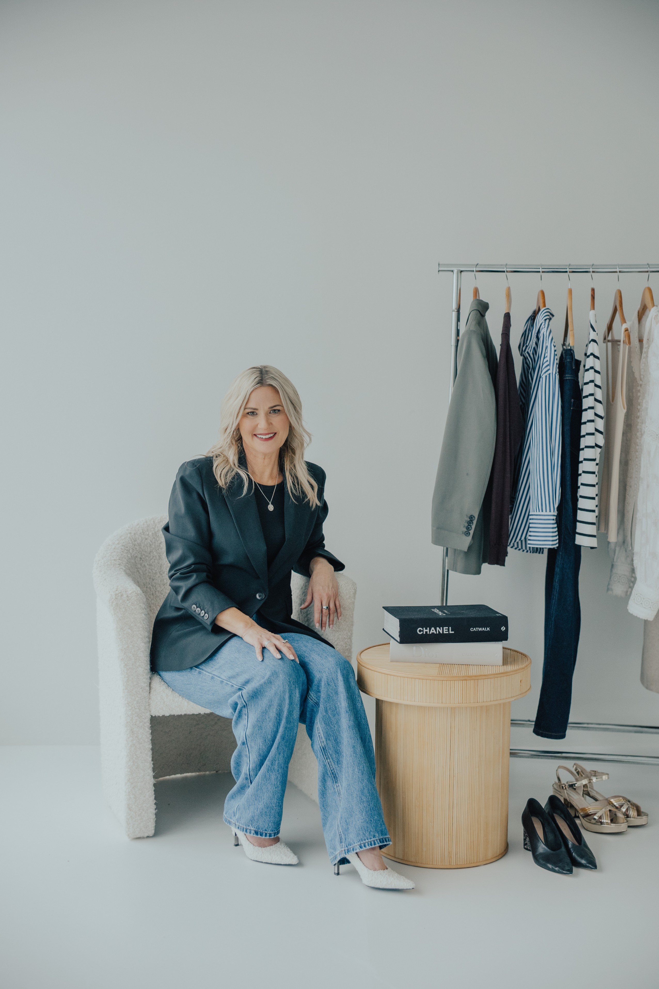Melissa Armitage Auckland personal stylist sitting beside a curated clothing rack with neutral wardrobe pieces and accessories