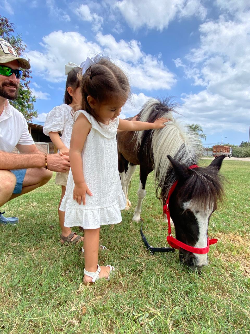 Padre y dos niñas acariciando un poni durante una tarde en familia en Fauné Finca Club, Manta