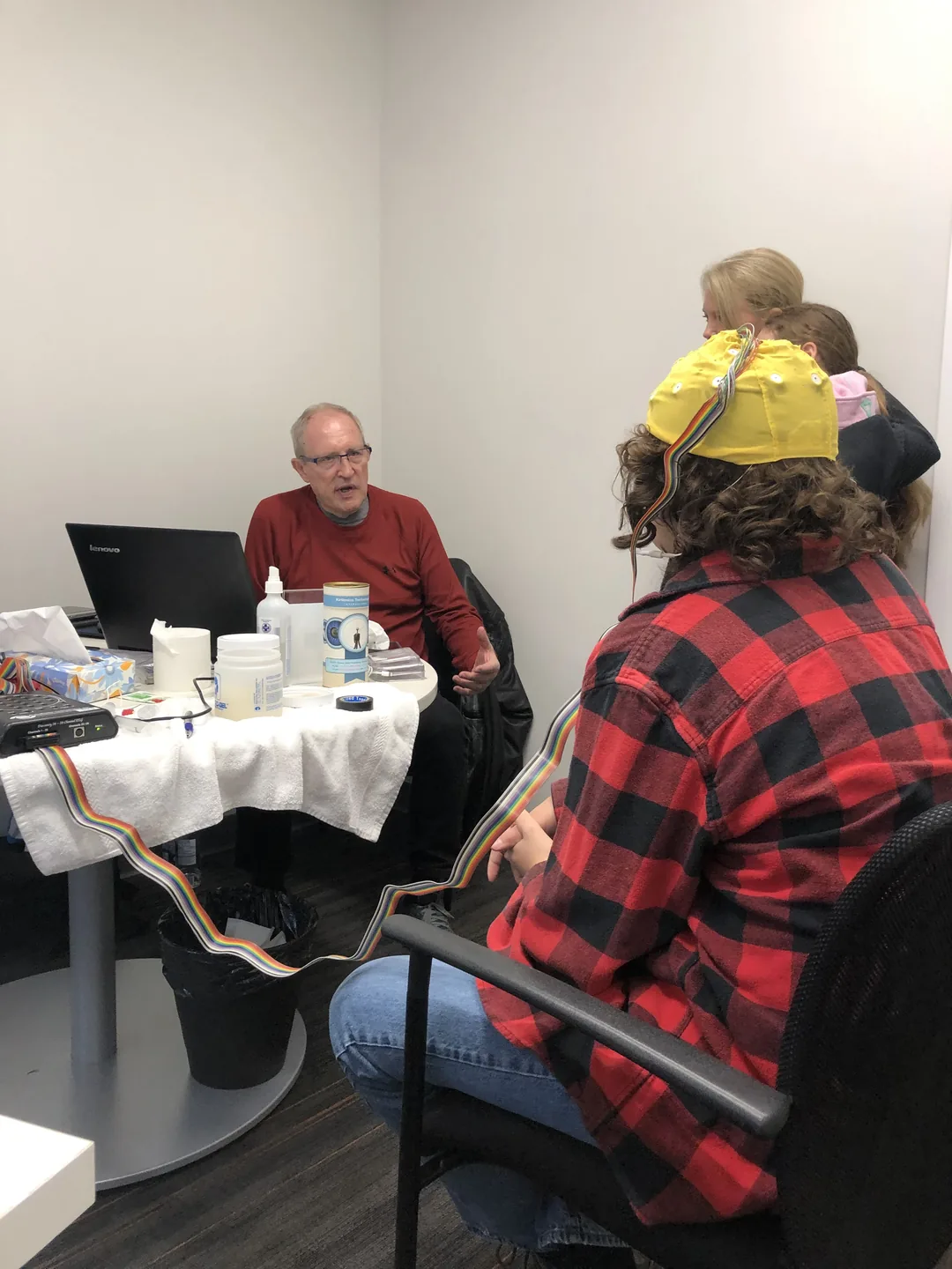 A participant in an EEG cap, with the readings on a laptop behind them
