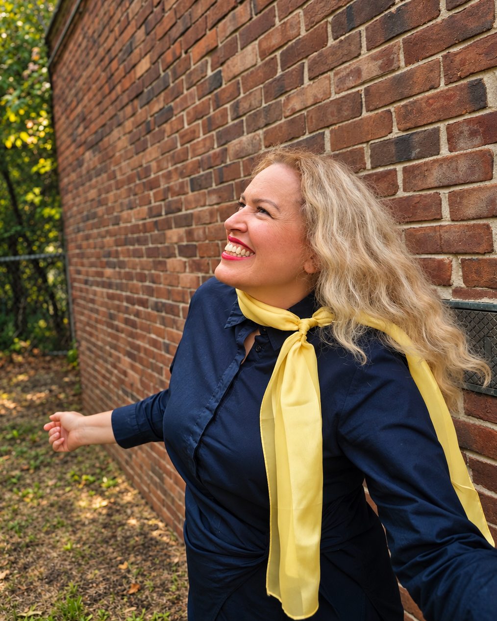 Mayra Sanchez laughing beside a brick wall, her gold scarf in the wind