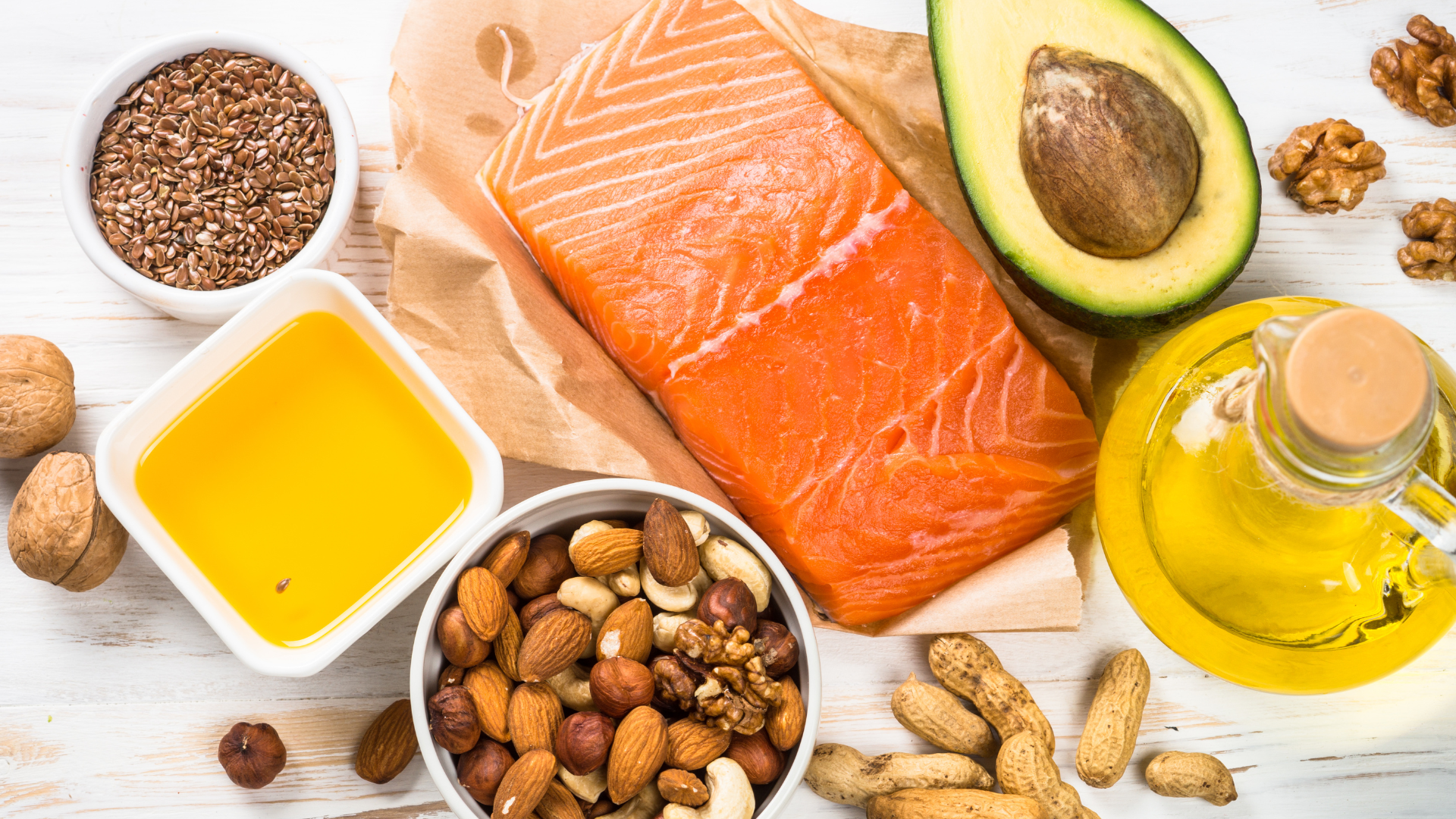 aw salmon fillet with avocado, nuts, seeds, and oil, arranged on a white table for a healthy fat diet.