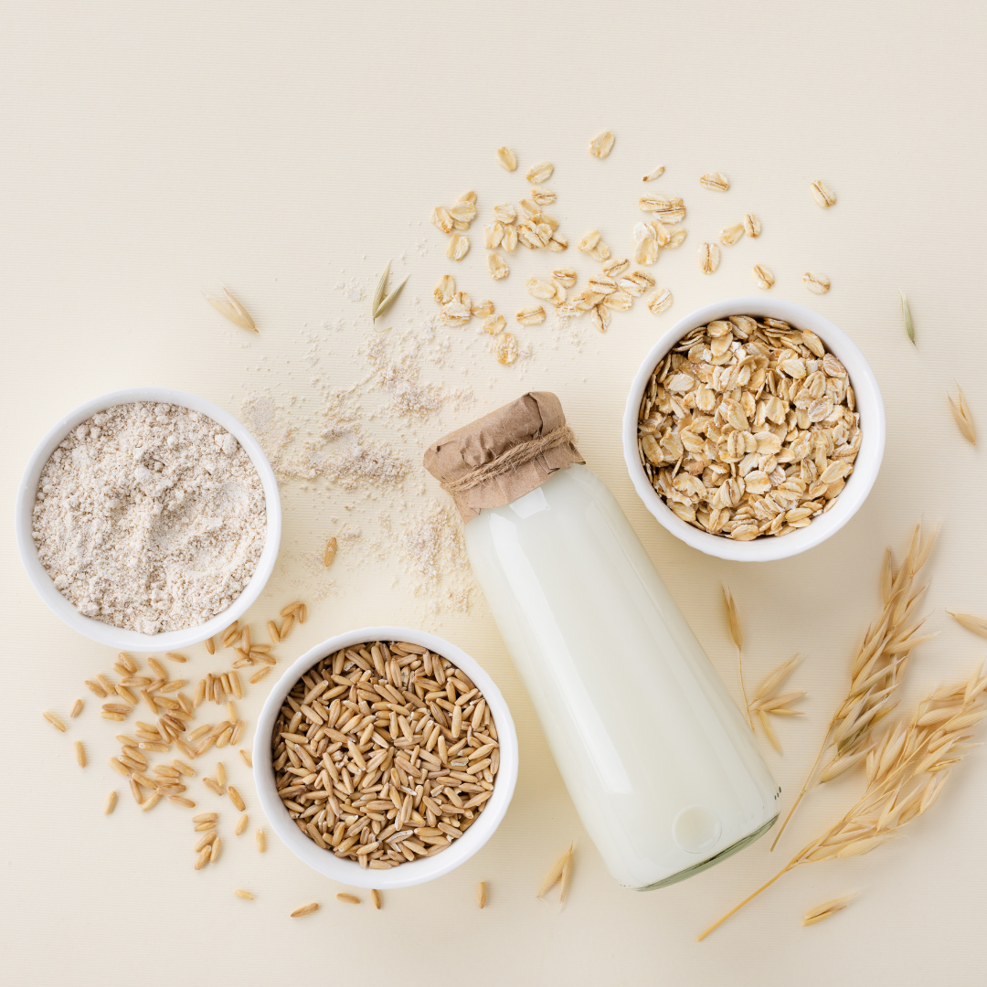 Oat milk bottle surrounded by oat grains, flour, and flakes on a cream-colored background.