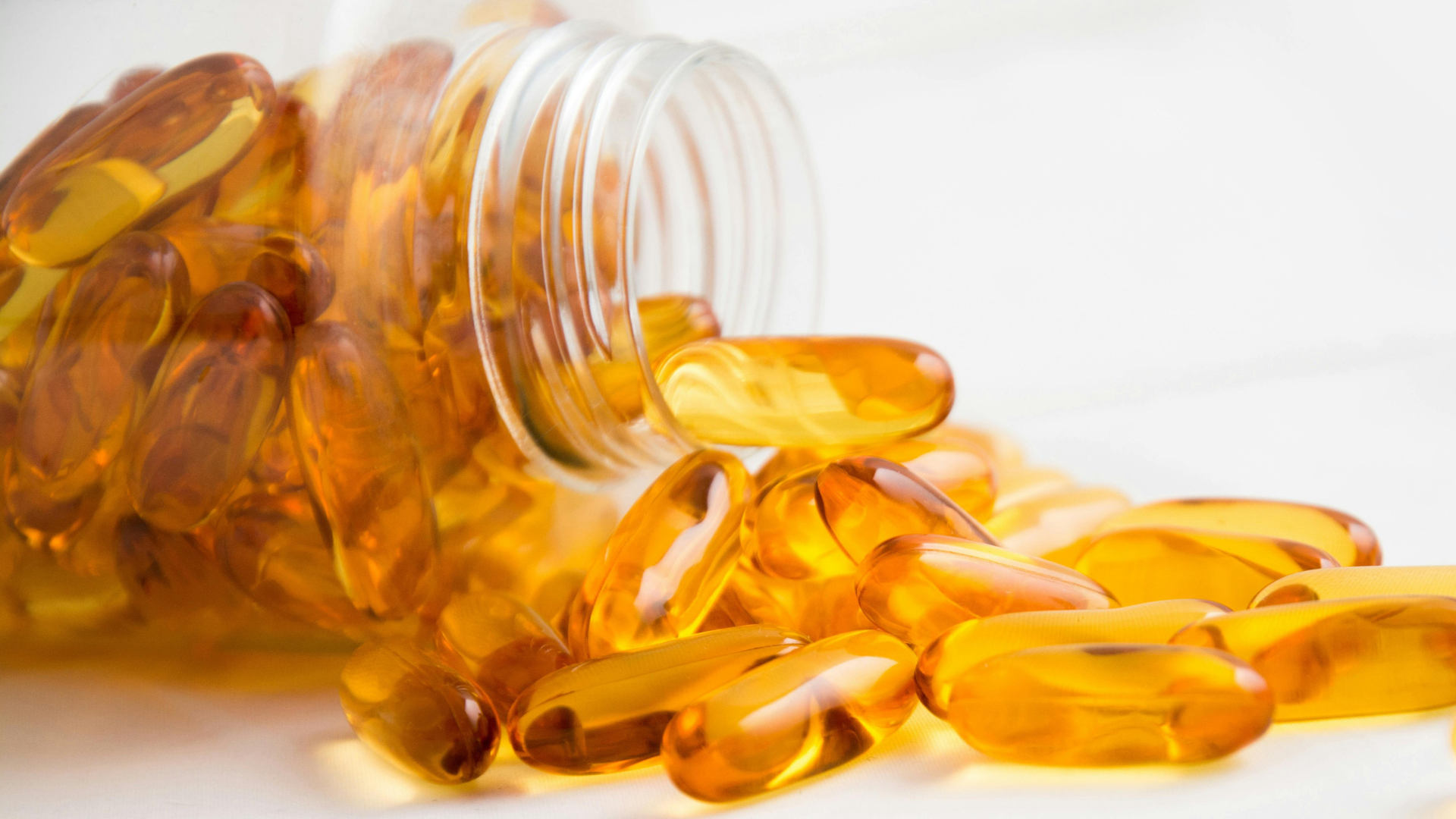 Open bottle with golden softgel capsules spilling out on a white surface.