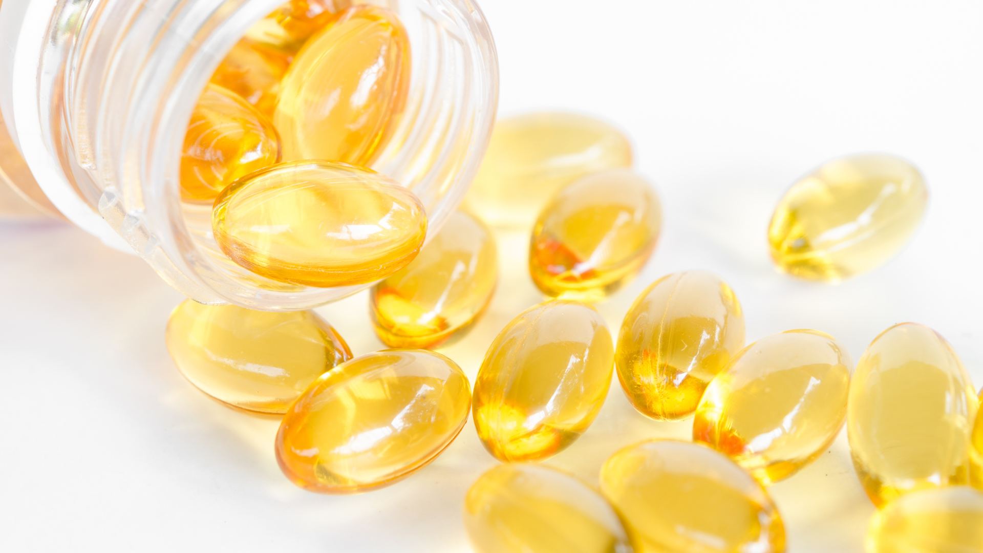 Yellow softgel capsules spilling from a clear bottle onto a white background.