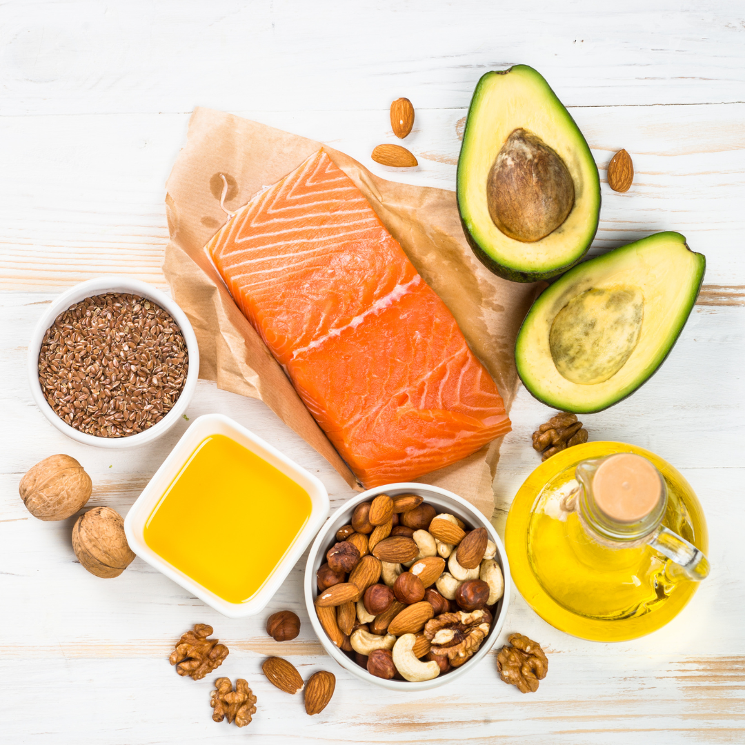 aw salmon fillet with avocado, nuts, seeds, and oil, arranged on a white table for a healthy fat diet.