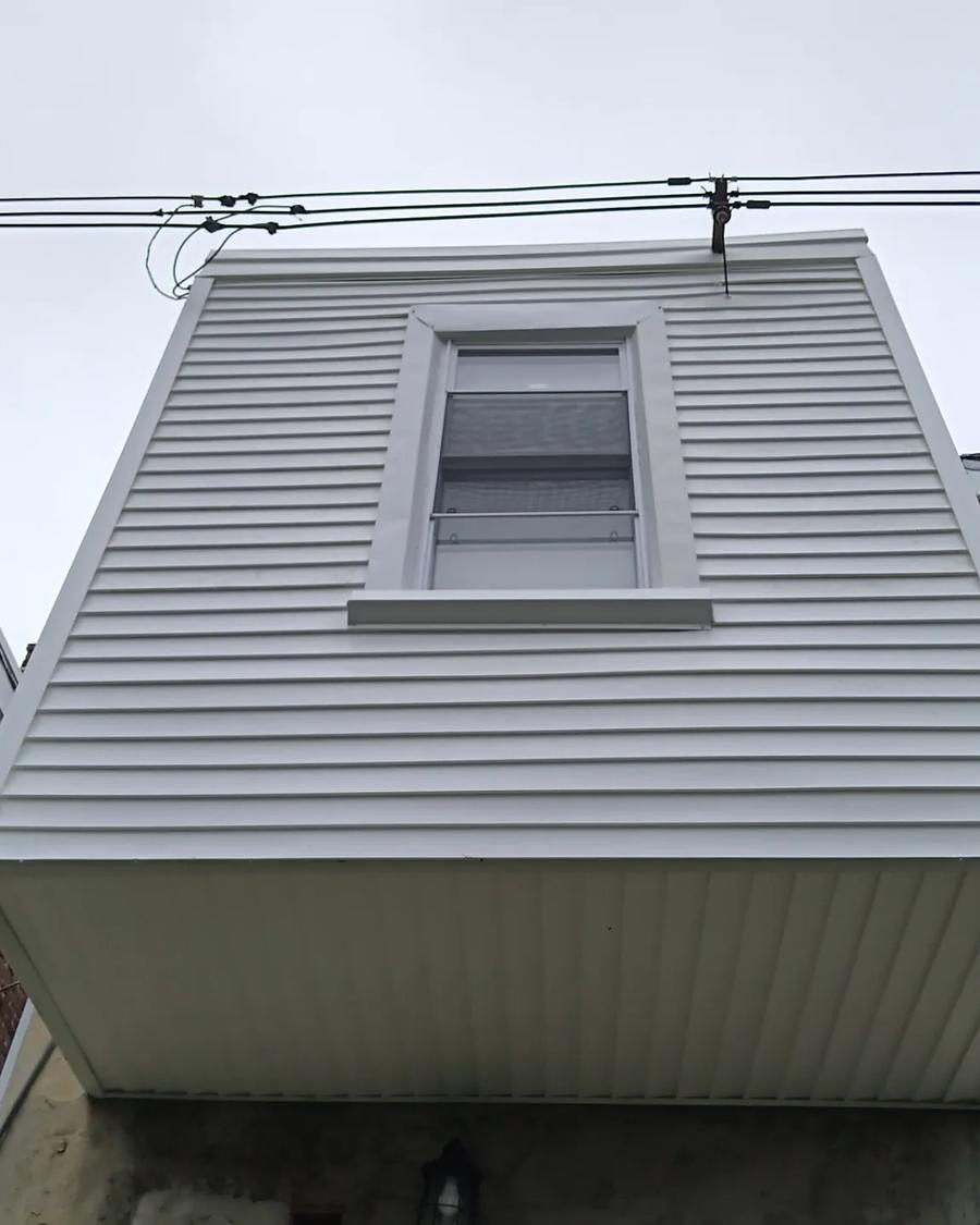 The same dormer wrapped in new white vinyl siding with a clean capped soffit