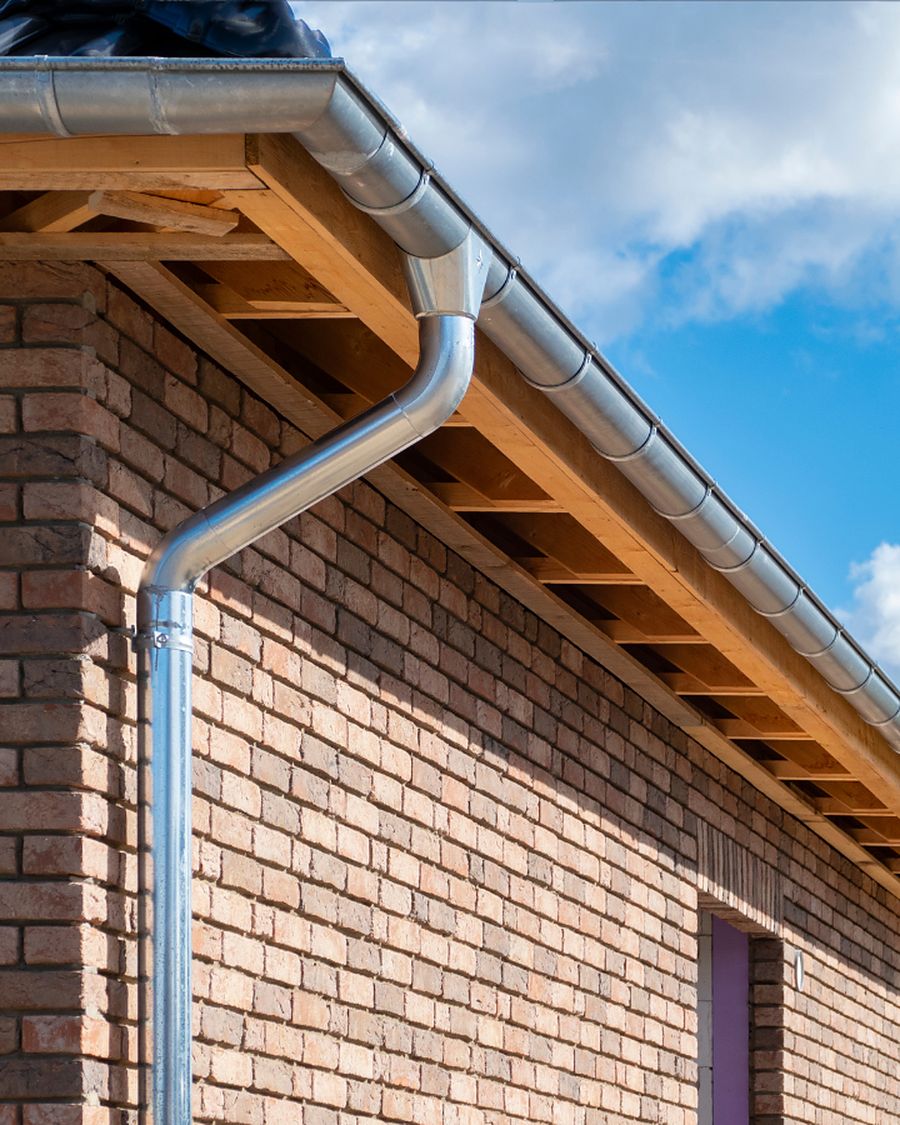 A seamless aluminium gutter and downspout running along a brick house