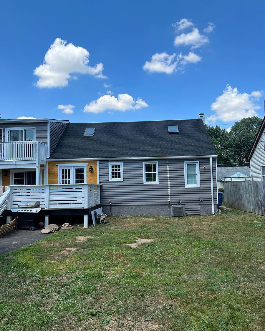 The rear elevation of the same cape, new shingle roof, skylights re-flashed and siding hung