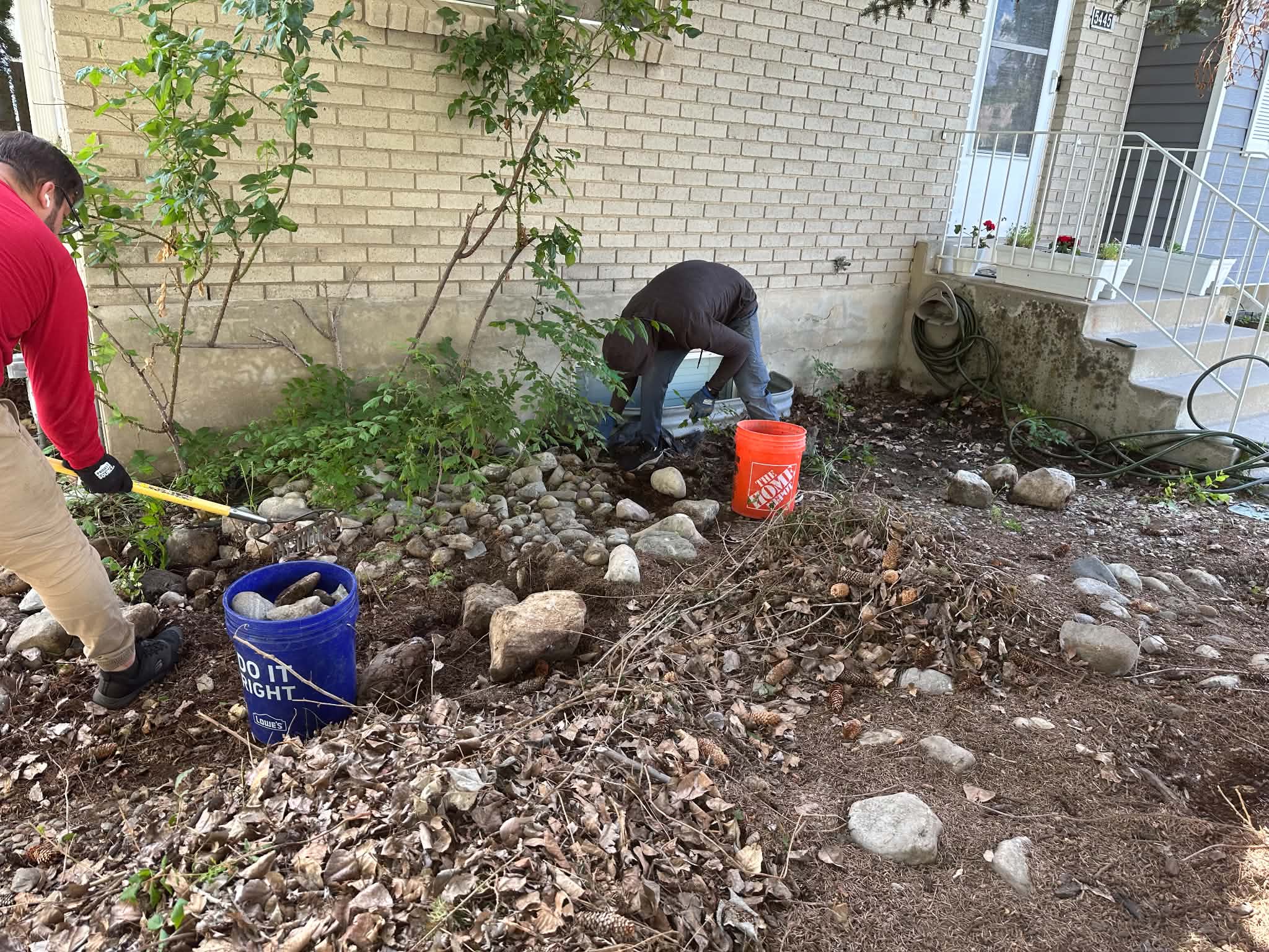 Two crew members working with rocks and plants near a house entrance