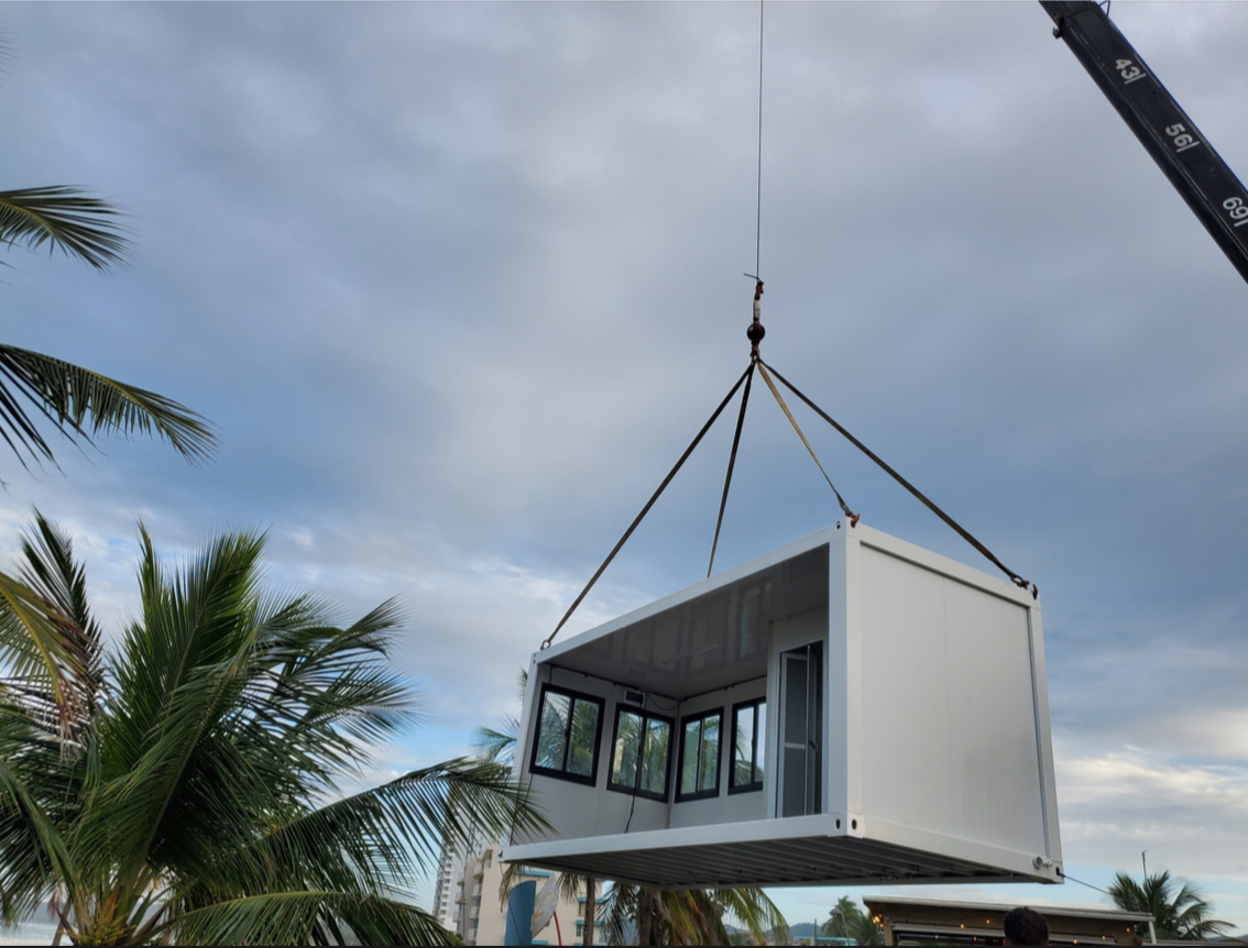 Modular home unit being installed by crane in Puerto Rico with palm trees in tropical setting Modular home unit being installed by crane in Puerto Rico with palm trees in tropical setting