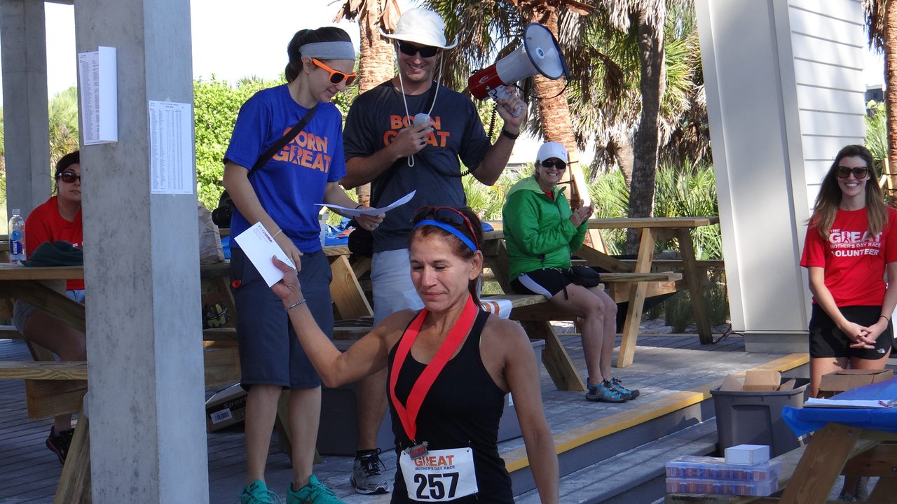 A finisher receiving her medal at The Great Mother's Day Race while volunteers cheer