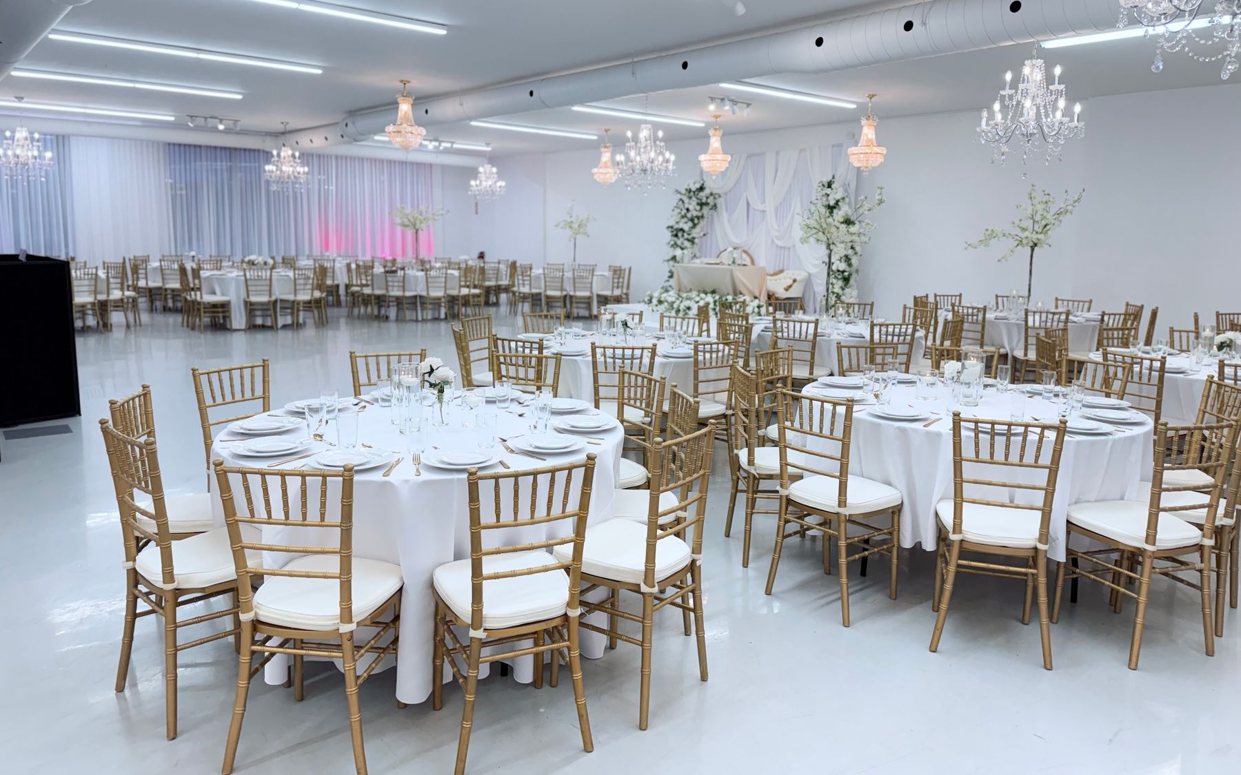 La salle dressée : tables rondes, chaises dorées et lustres de cristal