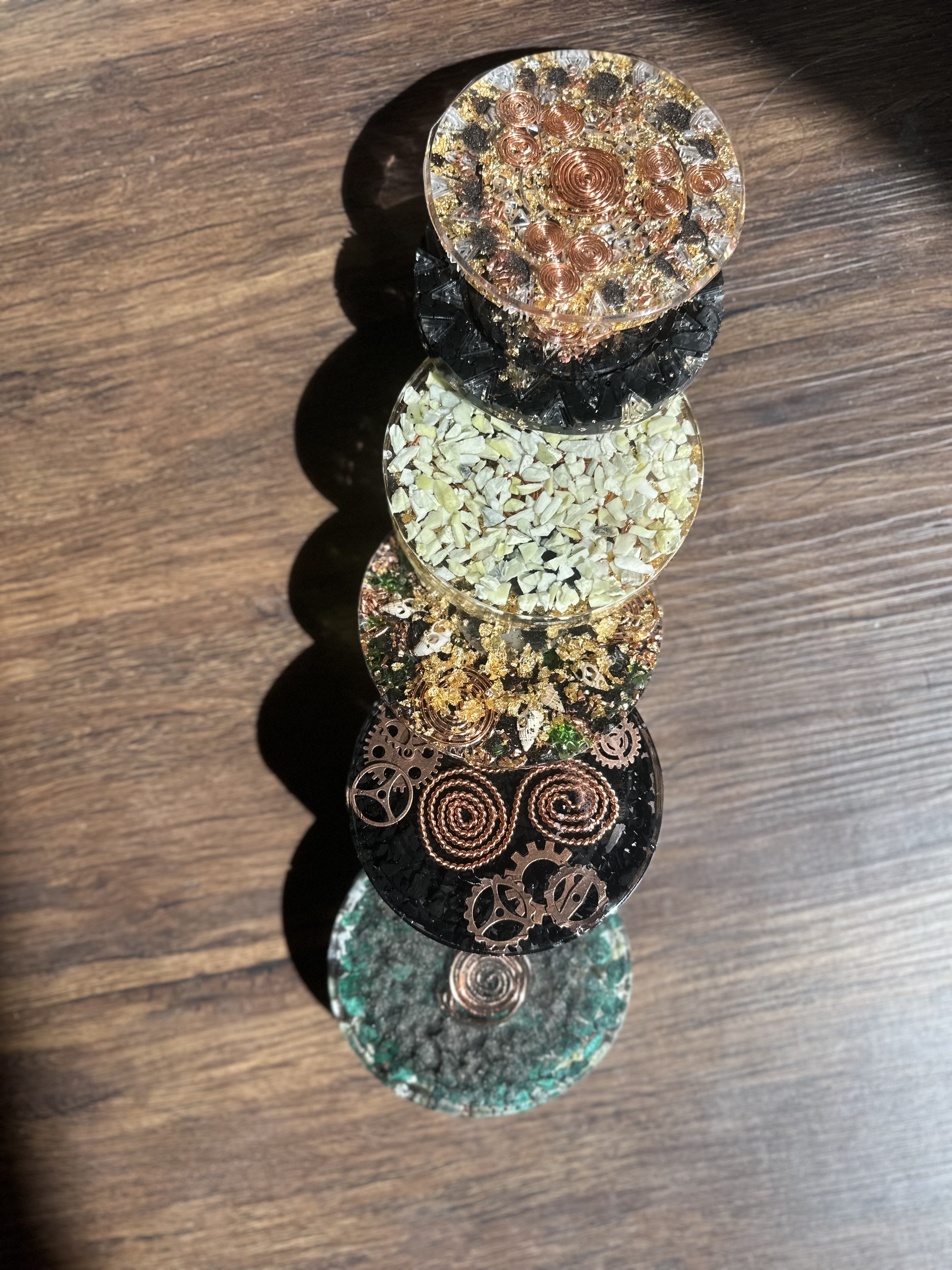 Five handmade orgone coasters in a row on dark wood, showing variety of designs with copper spirals, gold leaf, and sacred geometry patterns