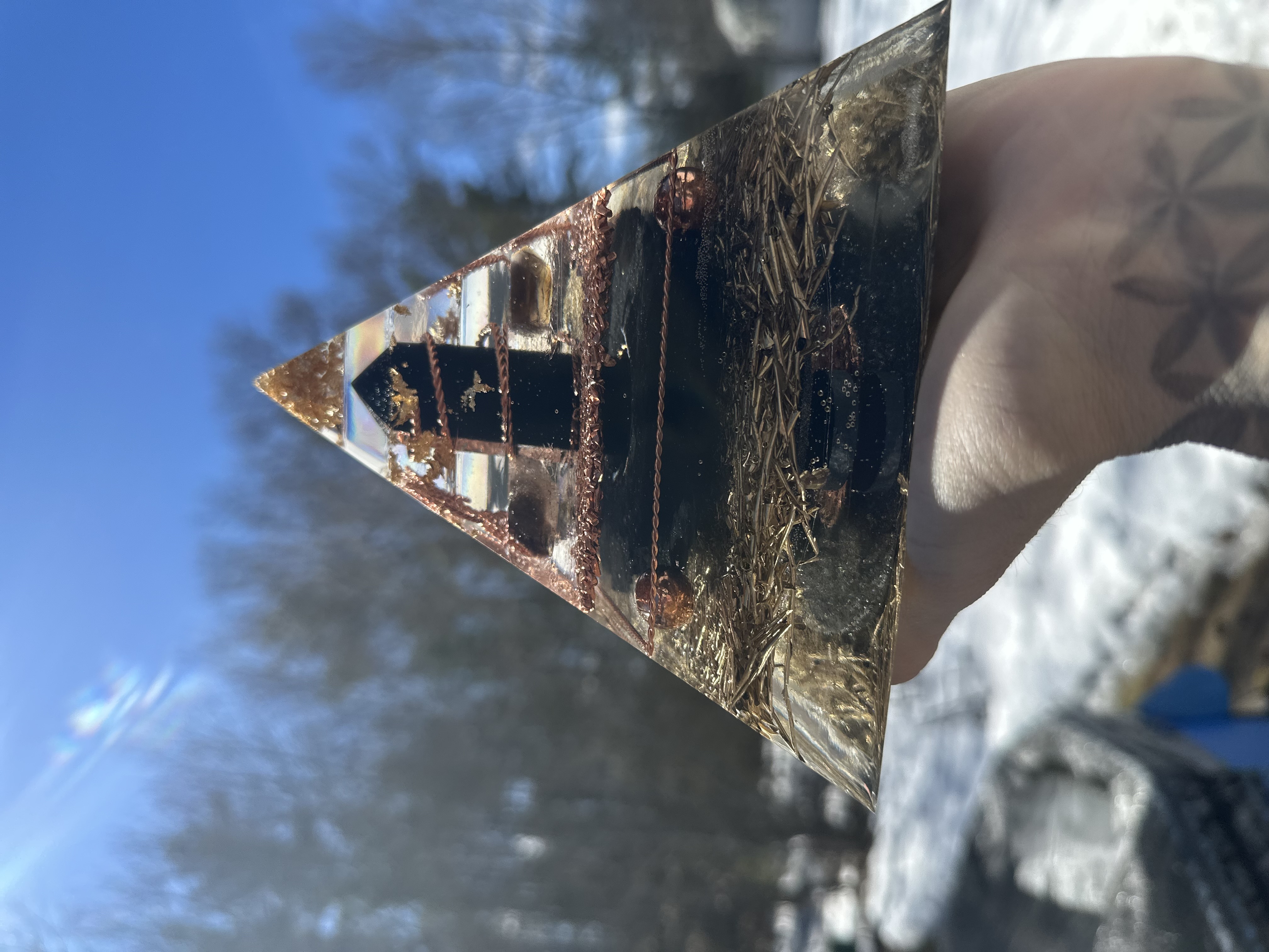Large orgonite pyramid held against sky showing light refraction