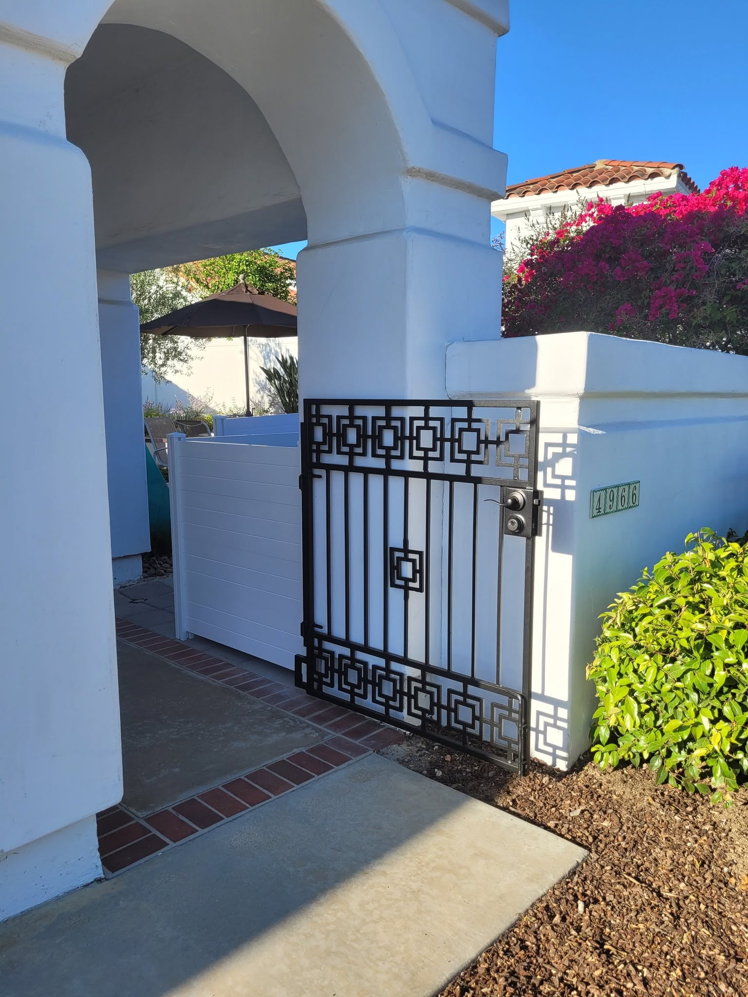 Geometric black iron pedestrian gate at a white residence