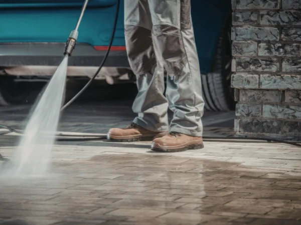 A person in work boots power washing a patterned stone patio with a concentrated stream of water.