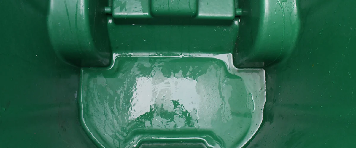 Close-up overhead view of a wet, dark green plastic surface with a rectangular indentation and hinge details. Close-up overhead view of a wet, dark green plastic surface with a rectangular indentation and hinge details.