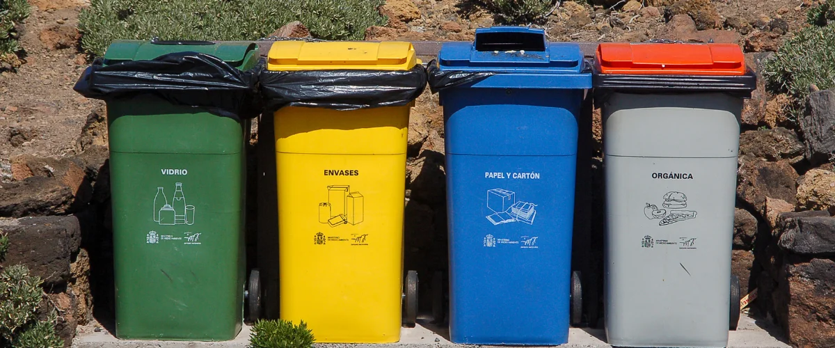 Four different colored recycling bins in a row against a rock wall, labeled in Spanish for sorting waste. Four different colored recycling bins in a row against a rock wall, labeled in Spanish for sorting waste.