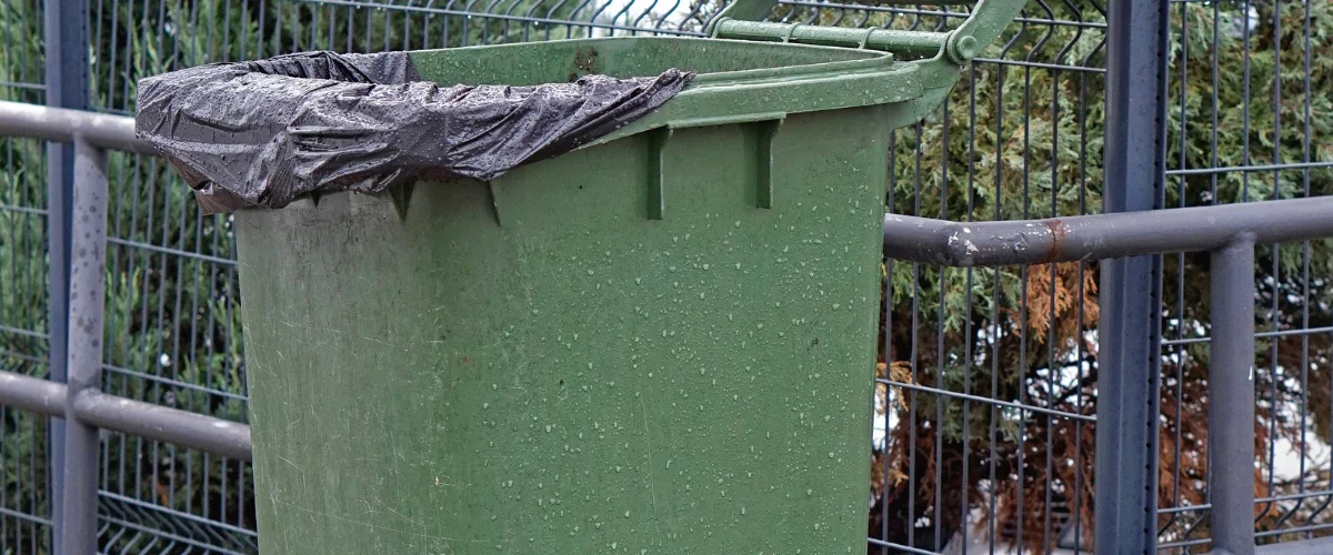 A close-up of a green plastic bin with a black trash liner over its rim, covered in water droplets. A close-up of a green plastic bin with a black trash liner over its rim, covered in water droplets.