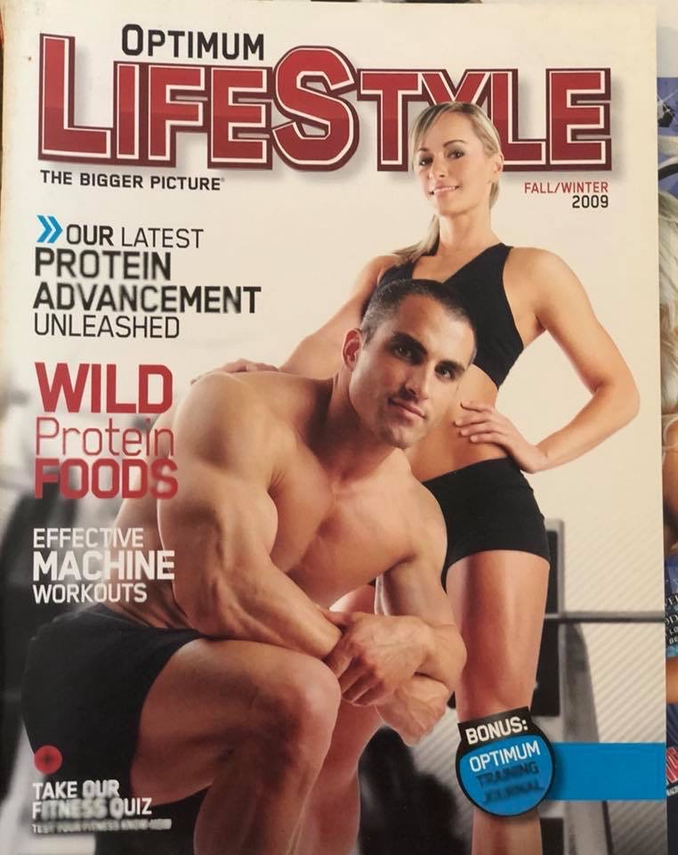 Optimum Lifestyle magazine cover featuring Tobias Young posing with a female fitness model.