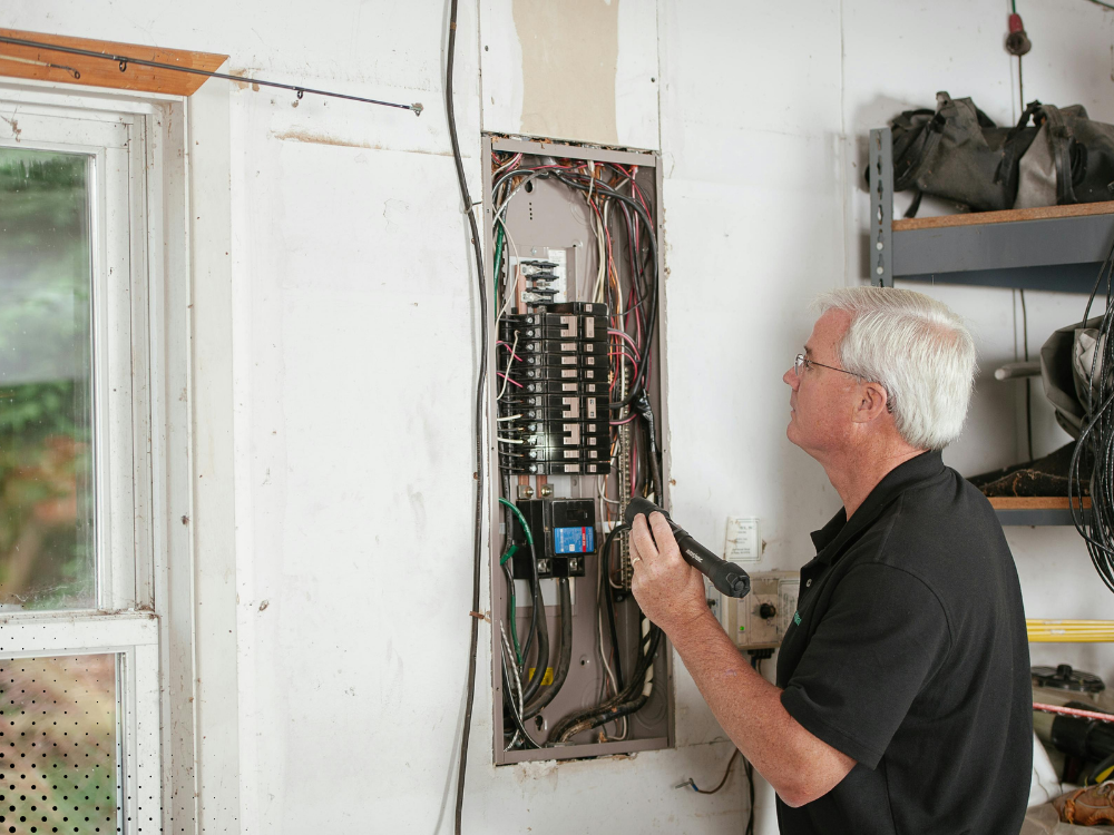 Home inspector examining an open electrical panel inside a garage or utility area.