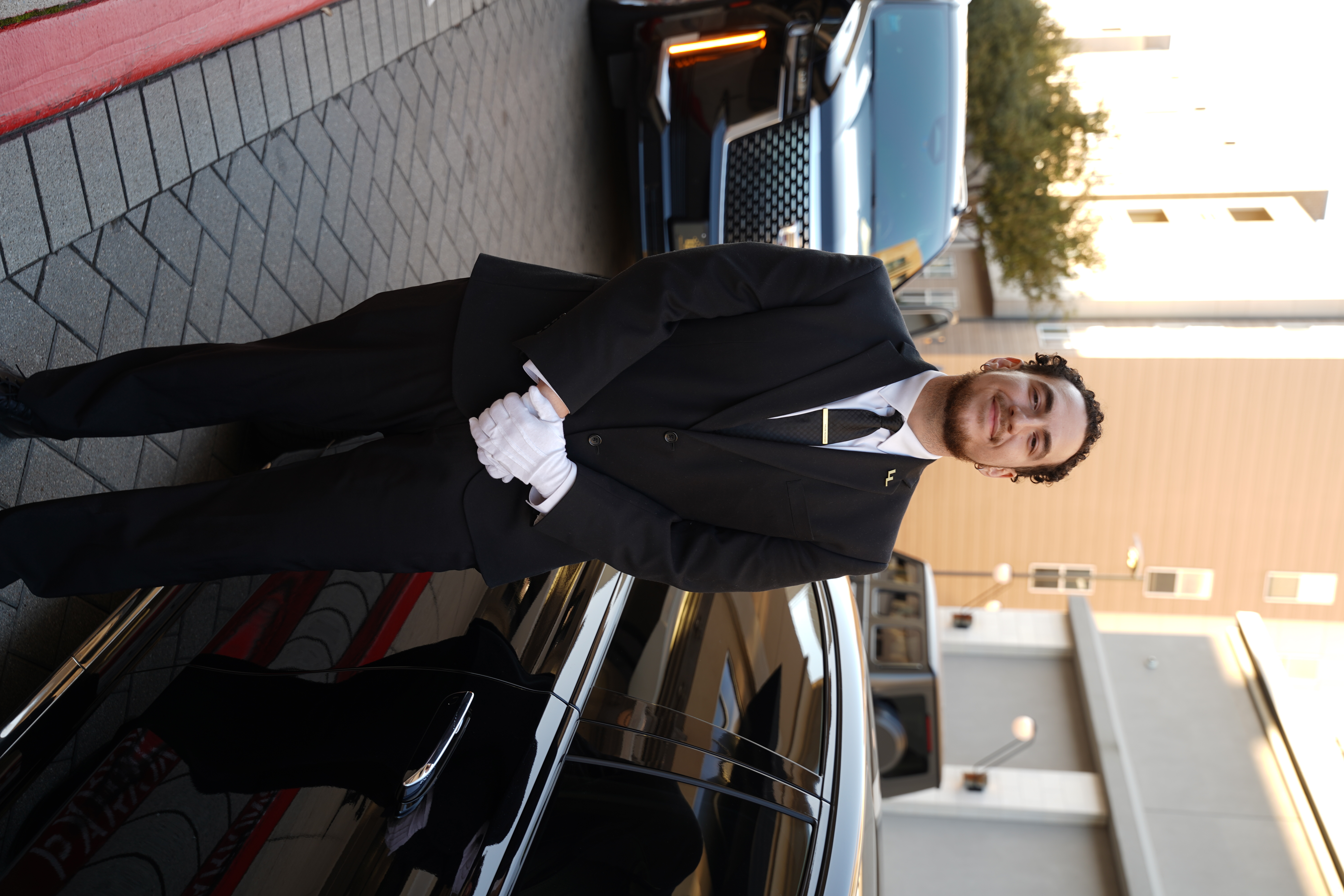 Professional private chauffeur in a tailored suit placing designer shopping bags into the rear trunk of a black luxury SUV.
