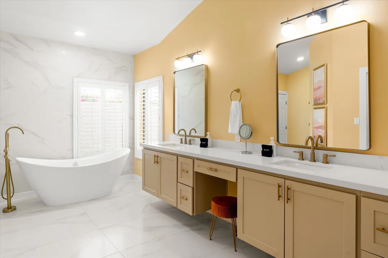 Primary bathroom with a freestanding tub, brushed gold fixtures and a double vanity by Logan Construction