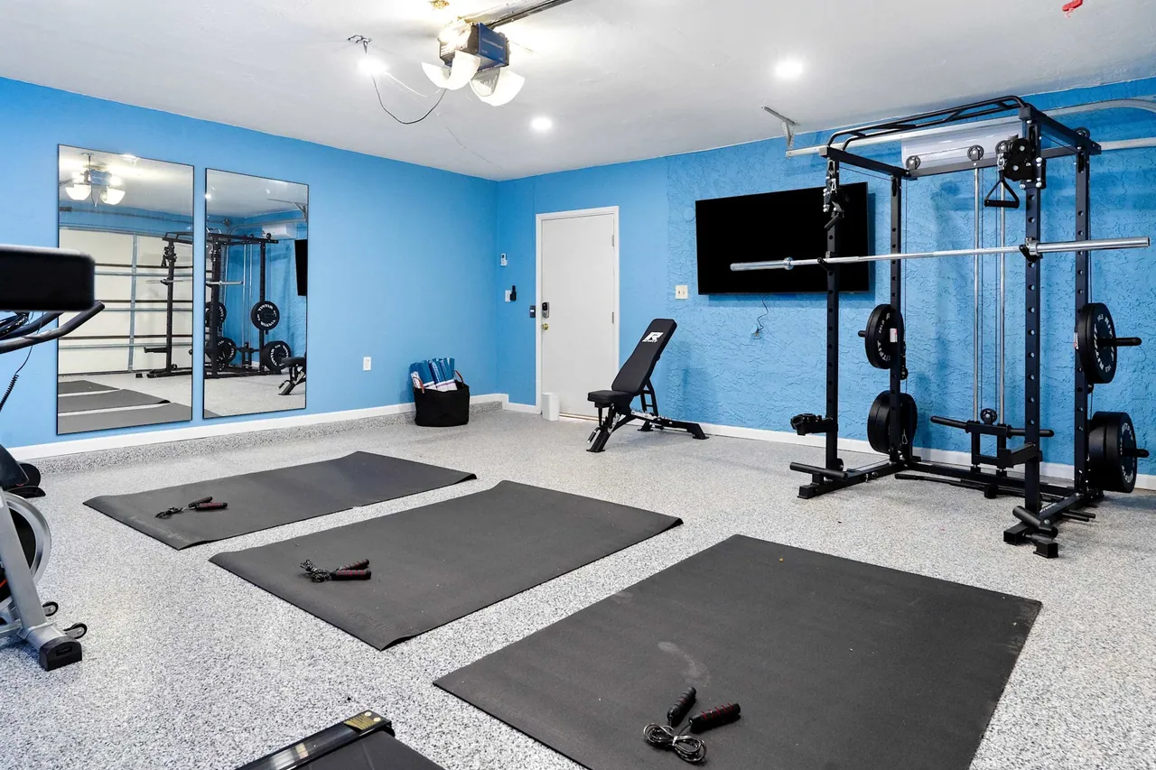 Garage converted into a gym with rubber flooring and a TV wall by Logan Construction