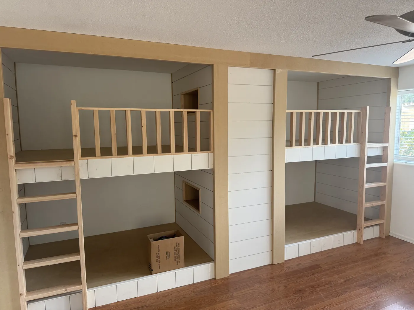 Built-in bunk beds mid-build, with shiplap walls, wood guardrails and ladders before paint