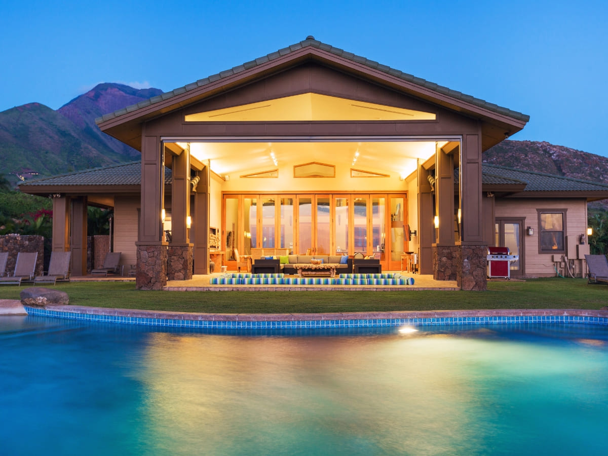 Modern poolside villa with expansive glass doors opening to a serene swimming pool under a clear evening sky.