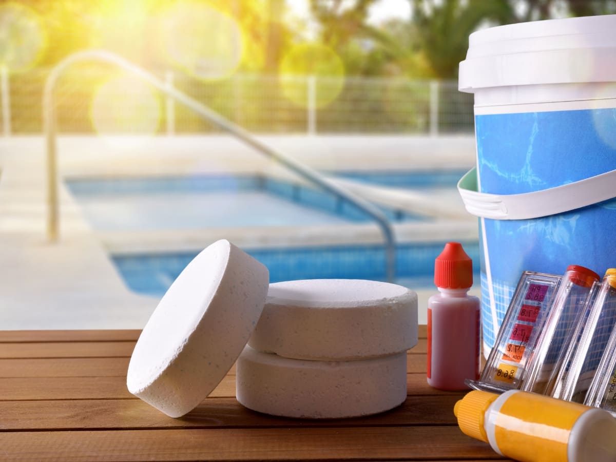 Pool cleaning chemicals and tools, including chlorine tablets and test kits, with a pool in the background in Baldwin.