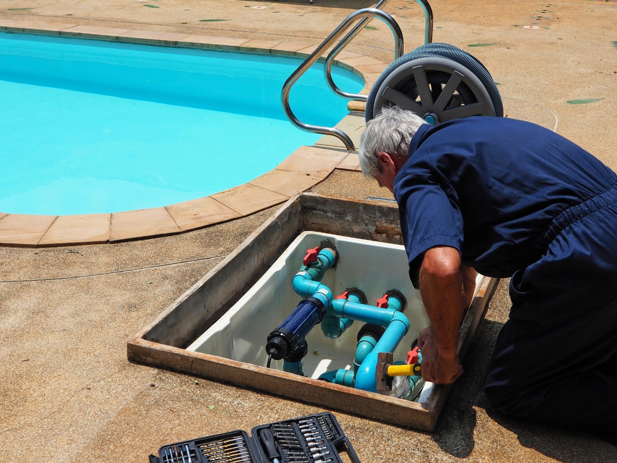 Pool technician performing maintenance on pool equipment beside a clean pool in Baldwin.