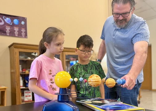 A Countryside teacher and students exploring a solar-system model together.