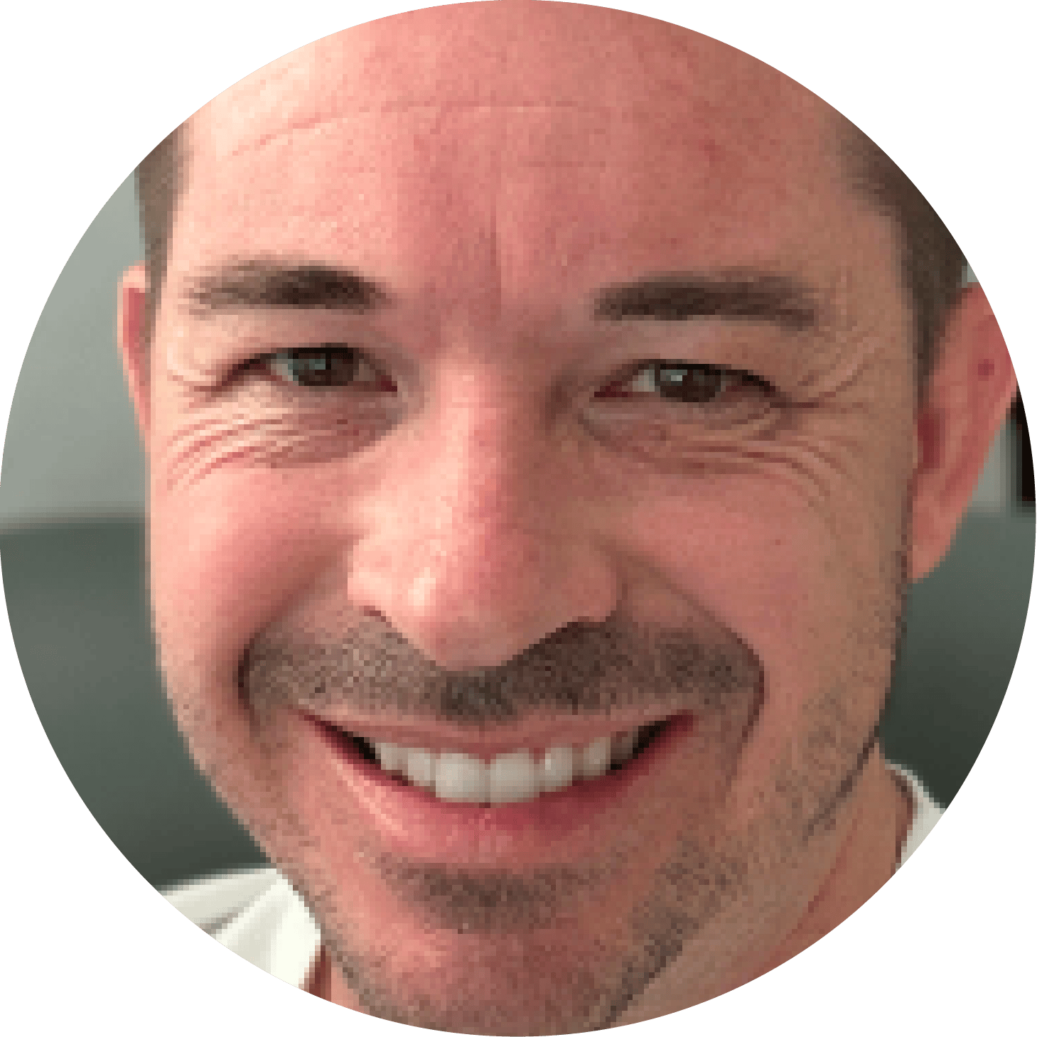 A close-up, circular portrait of a smiling man with brown eyes, short hair, and a slight beard.