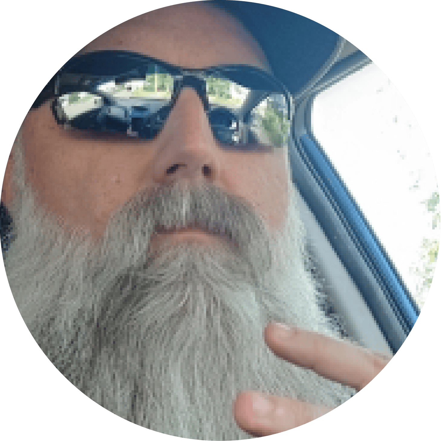 Close-up of a bearded man wearing sunglasses sitting inside a car.