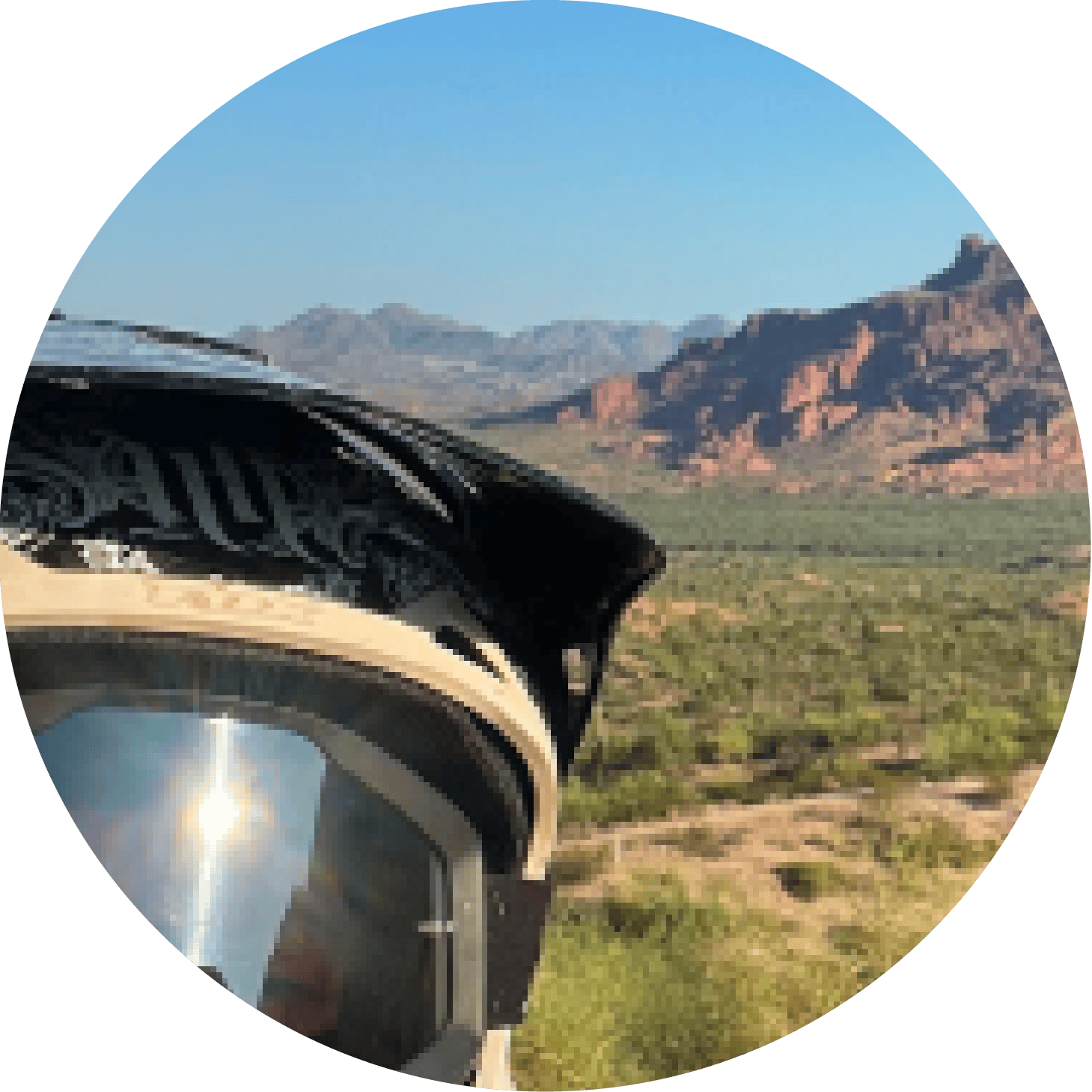 Car side mirror in foreground with desert shrubs and red mountains under clear blue sky.