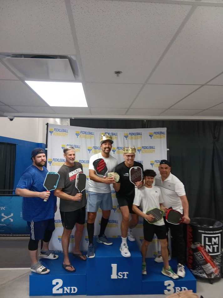 Tournament winners wearing gold crowns on the podium at Pickleball Kingdom