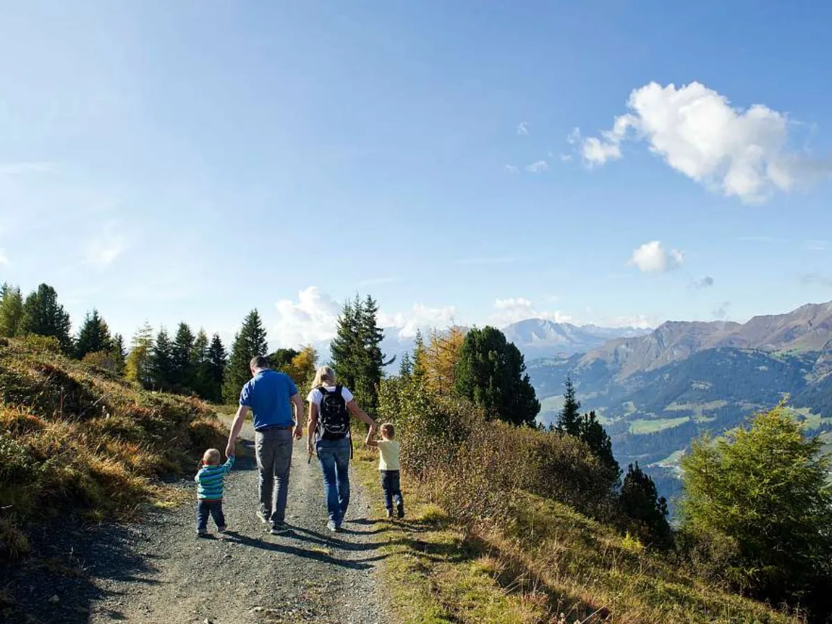 Familie mit Kindern auf dem Outdoor-Spielplatz des Sunstar Hotels Arosa bei Sonnenschein mit Bergpanorama
