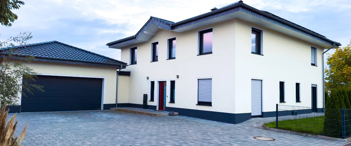 A modern two-story house with light yellow walls, black trim, an attached garage, and a grey paved driveway.