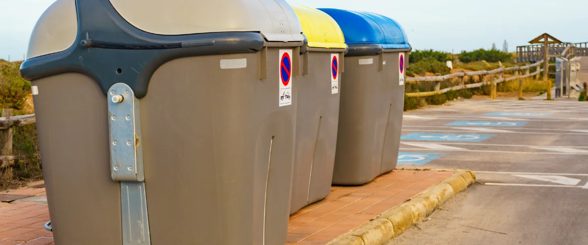 Three large recycling bins with yellow and blue lids next to a parking lot with blue handicap symbols. Three large recycling bins with yellow and blue lids next to a parking lot with blue handicap symbols.