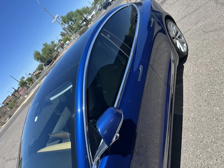 Close-up of the tinted front driver window and mirror on a blue sedan in Arizona sunlight