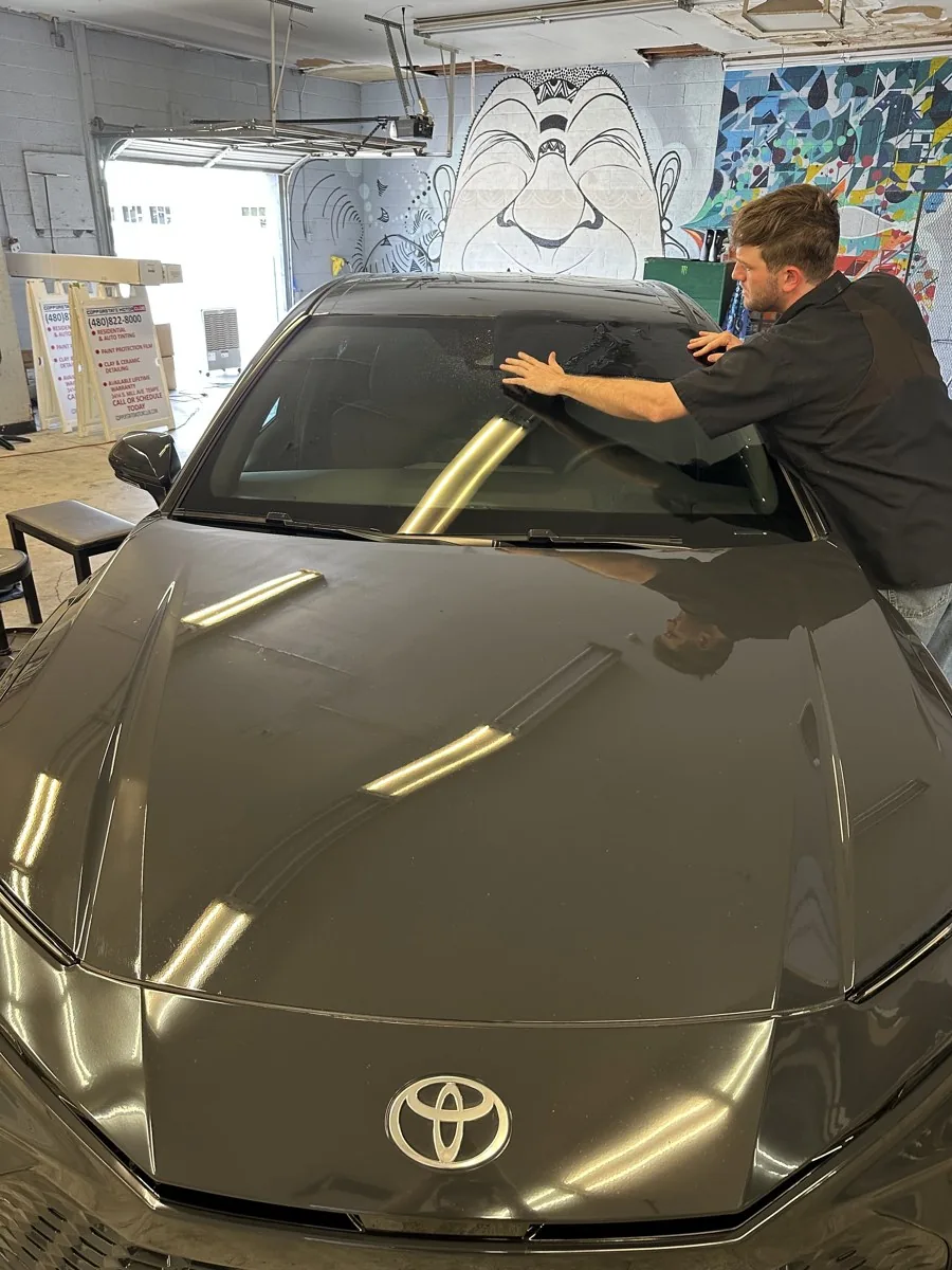 Copperstate technician squeegeeing pre-cut ceramic film onto a Toyota windshield inside the Tempe shop