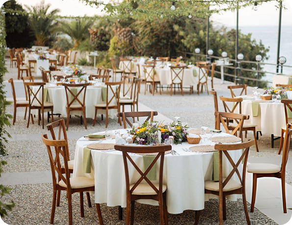 Outdoor event with round tables, white linens, and wooden cross-back chairs