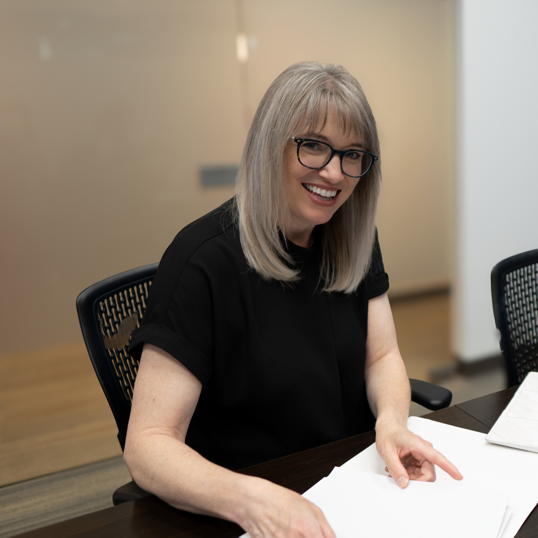 Edmonton realtor Cathy Cookson smiling at her desk, with a laptop and paperwork in front of her.
