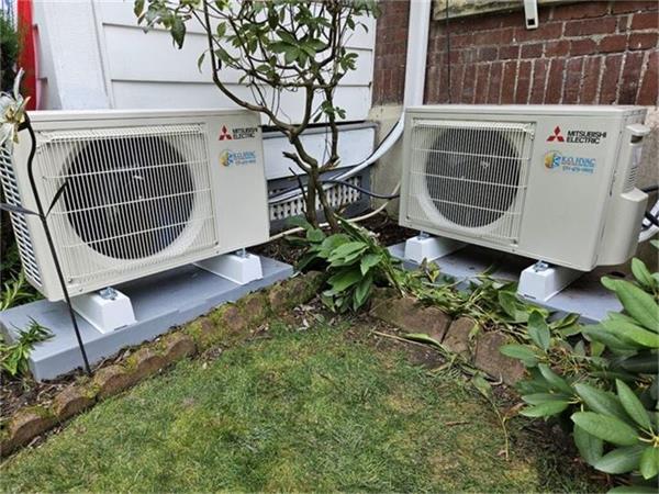 Two Mitsubishi Electric ductless condensers installed side by side on pads beside a brick home