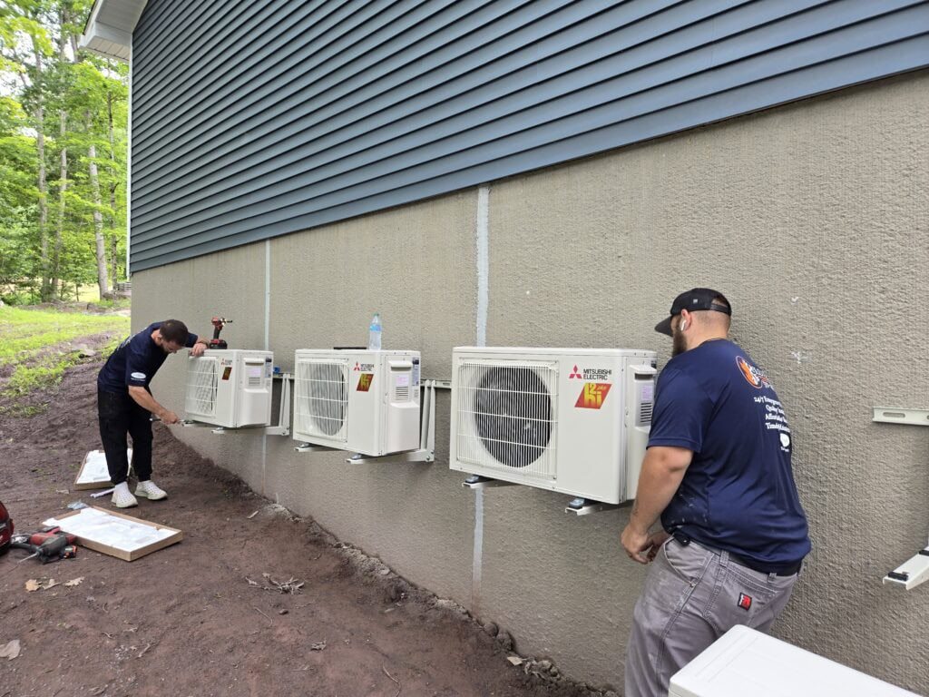 Two K.O. HVAC technicians in company shirts installing a row of Mitsubishi Electric ductless condensers on a home in the Wyoming Valley, Pennsylvania