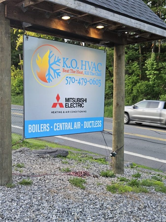 K.O. HVAC yard sign on a customer's lawn reading Boilers, Central Air, Ductless with the Mitsubishi Electric badge