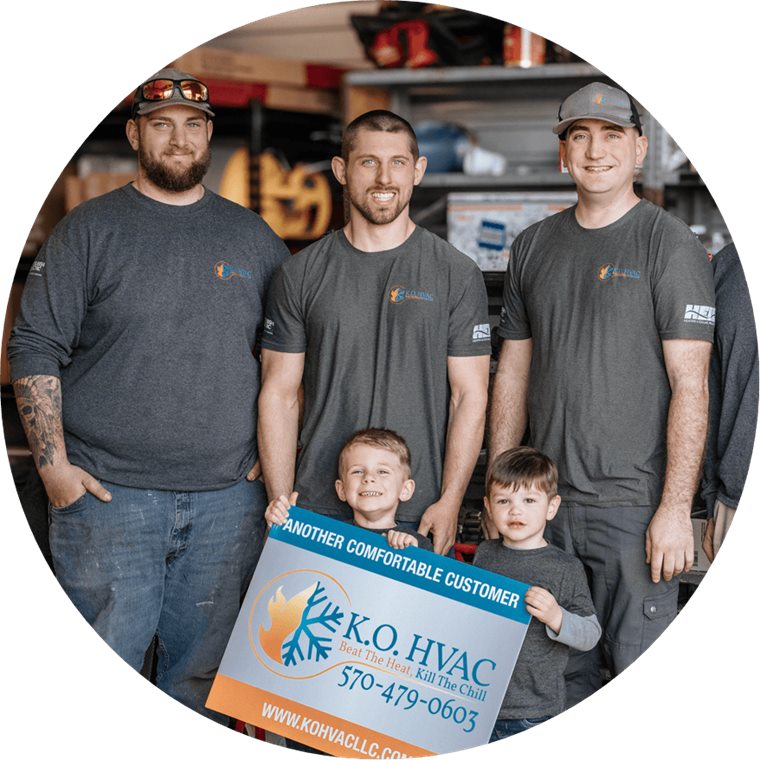 The K.O. HVAC crew in company shirts at the Kingston shop, with two children holding an Another Comfortable Customer sign