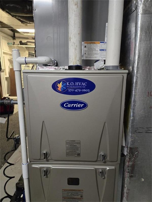 Carrier heating unit in a basement with a K.O. HVAC service sticker on the cabinet